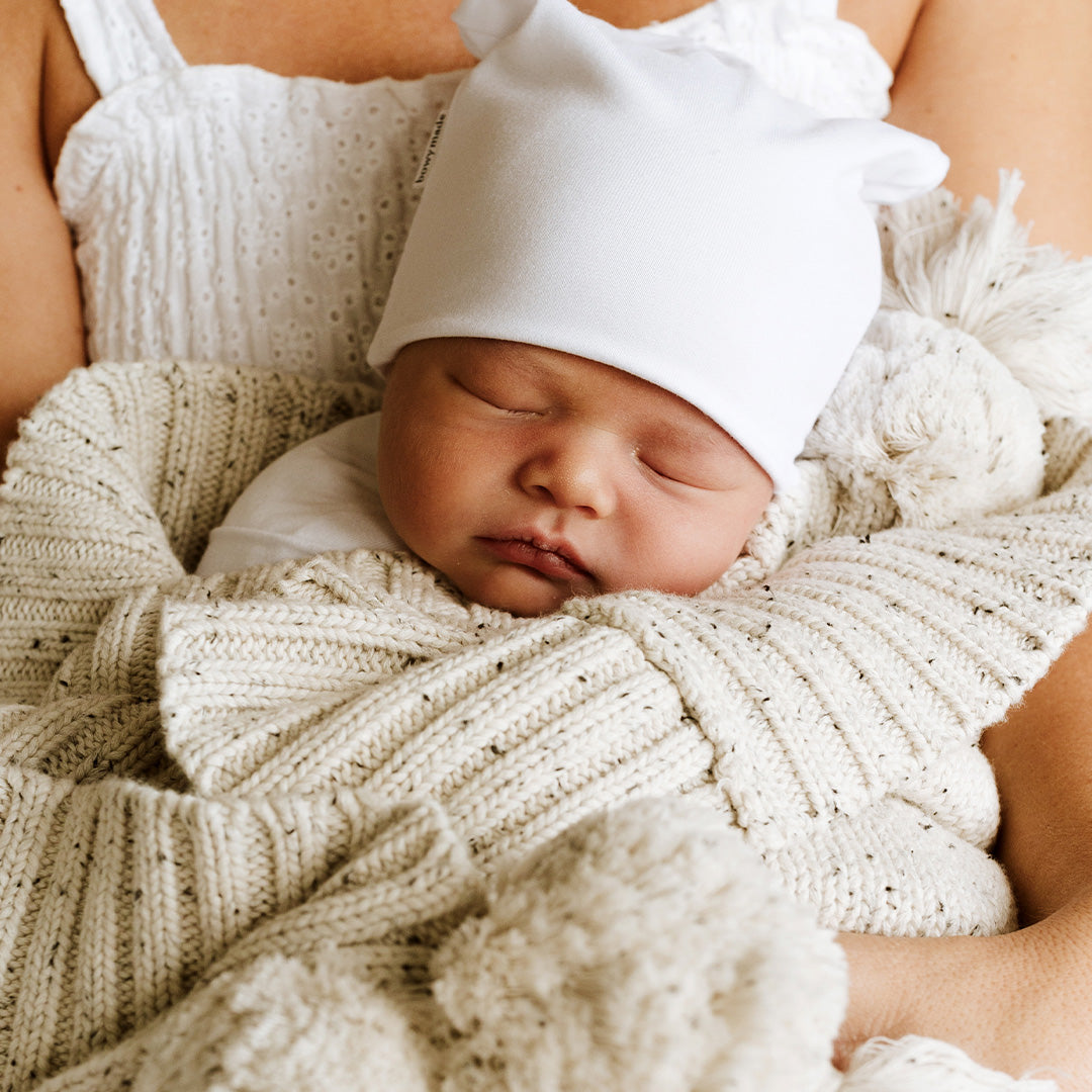 Baby wrapped in blanket wearing white slouch beanie