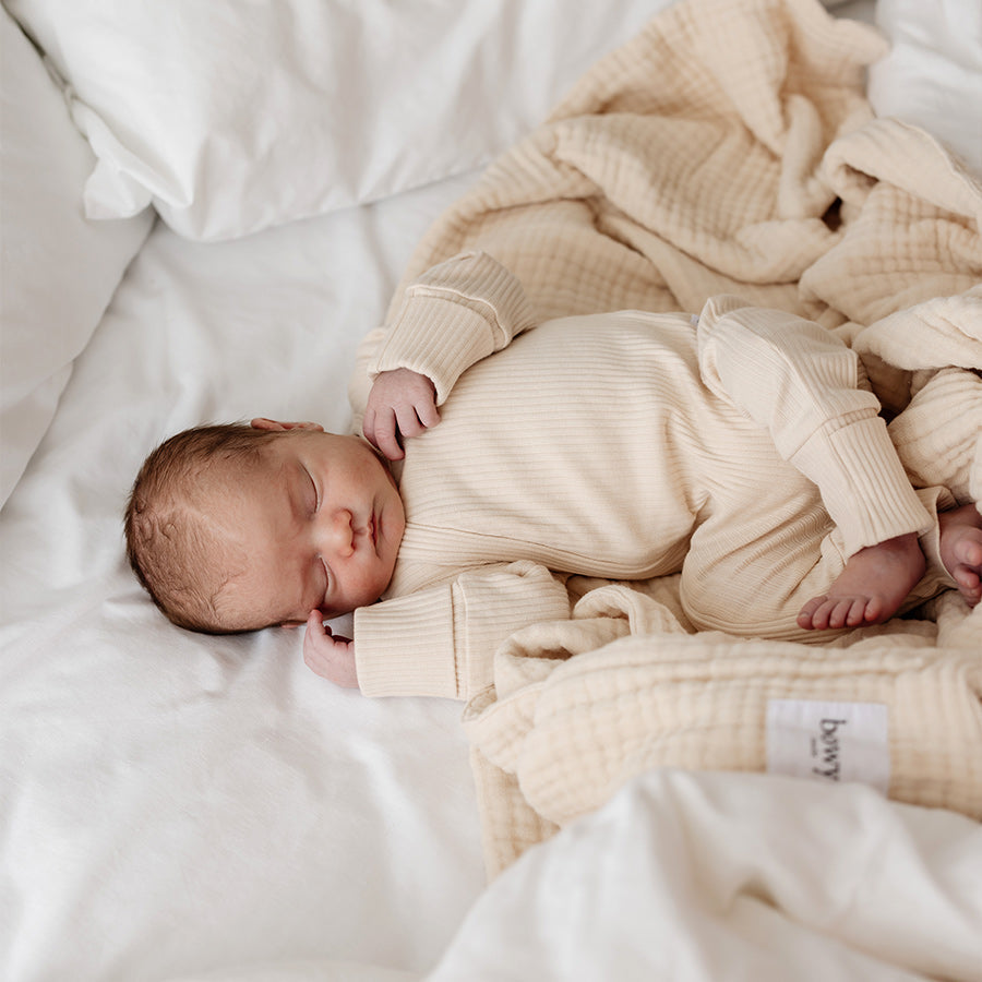 baby wearing neutral cream onesie, lying on thick cream  muslin baby blanket