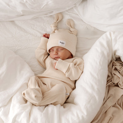 Baby wearing matching ribbed cotton onesie and beanie with two cute knots