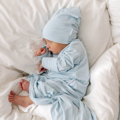 baby boy lays on white donna setting wearing matching blue Bowy Made brand gown and slouch beanie