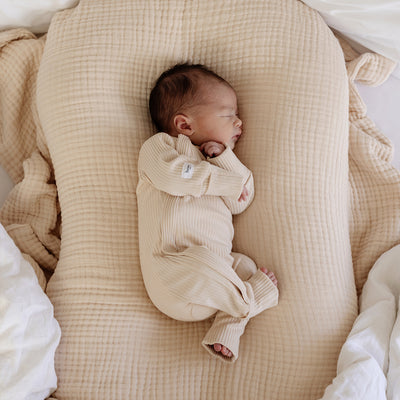 beautiful baby laying comfortably on a cream bubble blanket wearing a Bowy Made branded one piece suit of the same colour.