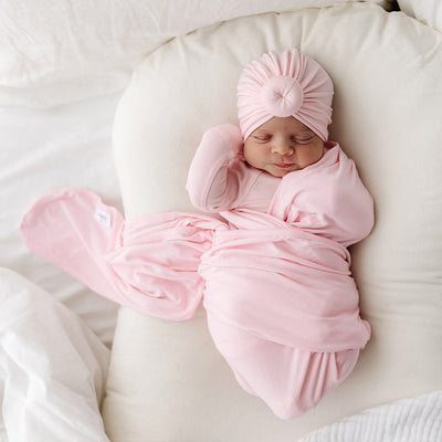 baby wearing all pink with a matching traditional turban with stylish front knot, sleeping blissfully on a white pillow