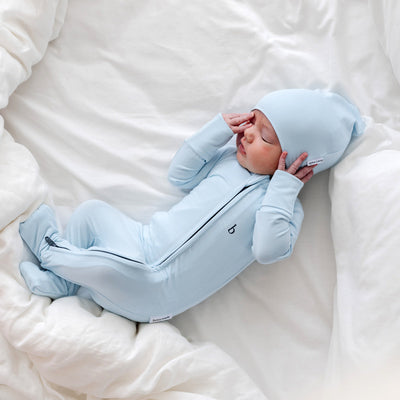 newborn baby holding his hands in front of face looking comfortable in matching sky blue zippy and beanie