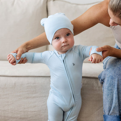 Toddler standing while being held by mother wearing a matching viscose slouch beanie and onesie in blue. 