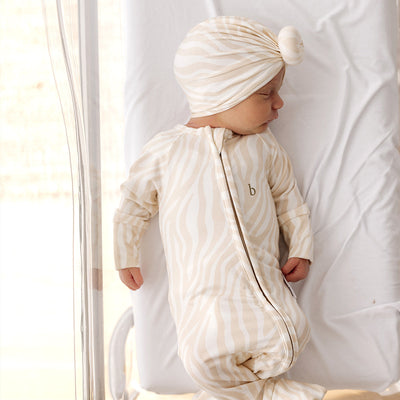 baby quietly sleeping in basinet wears a turban with a front bun in an animal print wearing a onesie of the same colour. 