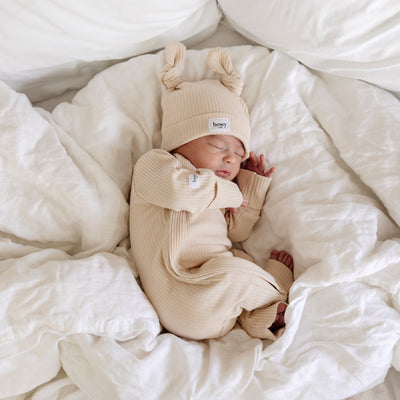 cute baby asleep in cream ribbed onesie and wearing the matching cream ribbed double knot beanie 