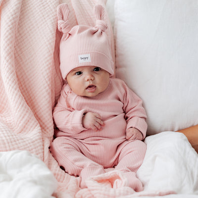 3 month old baby girl wearing matching ribbed cotton set in Pink. Sitting upright against light pink blanket.