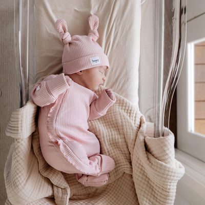 Cute baby wearing pink frill onesie set on cream blanket