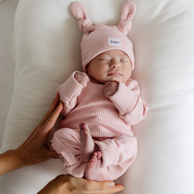 Baby laying on pillow wearing dusty pink ribbed set with hands