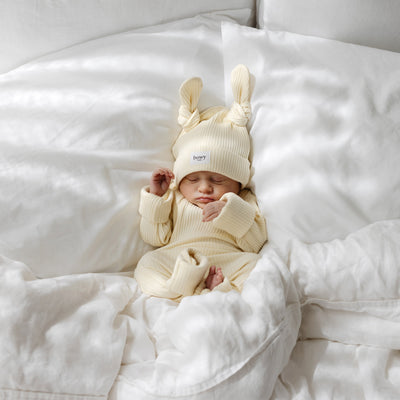 Newborn baby in a yellow-coloured outfit with double knot beanie on a white blanket