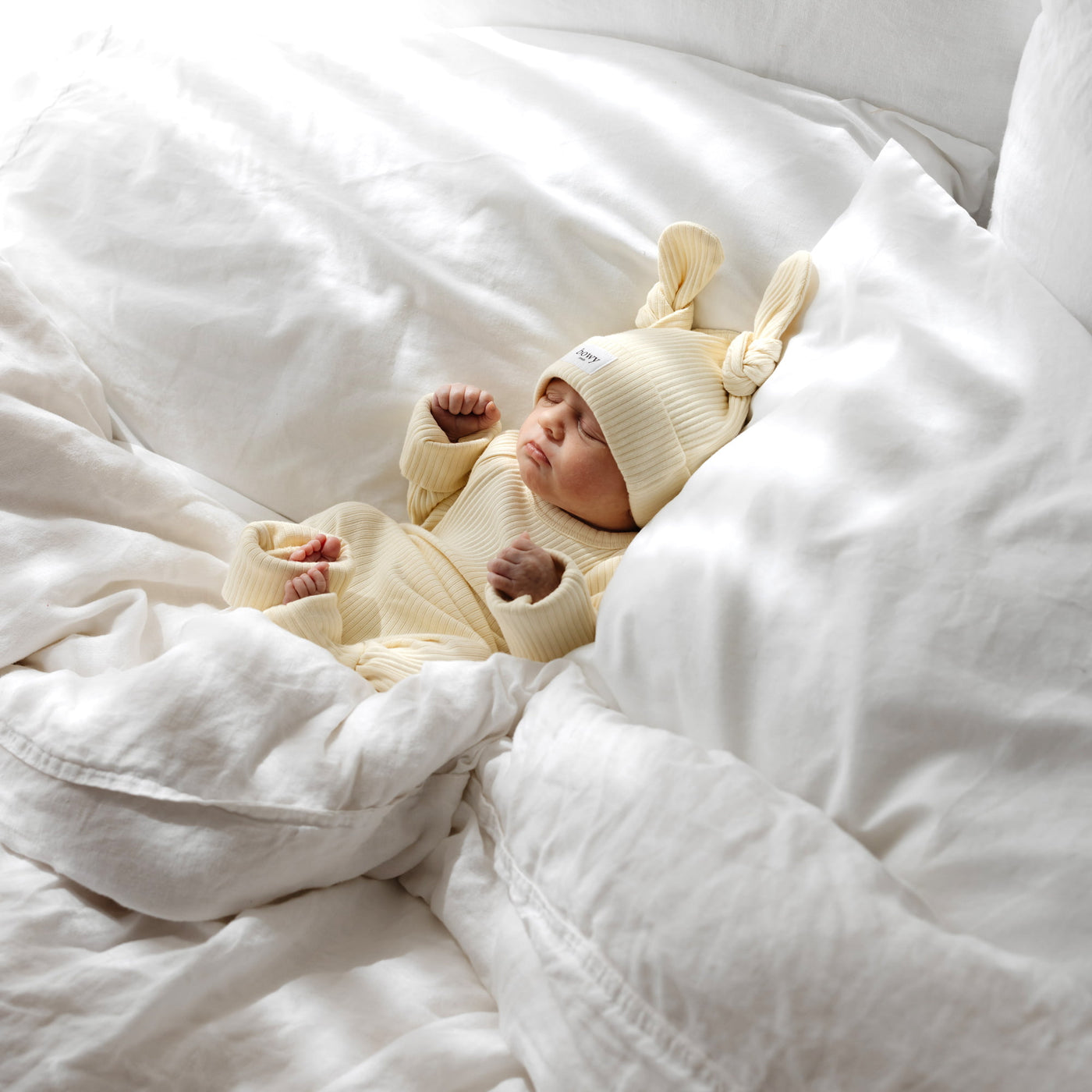 Baby in a lemon-colored outfit and hat lying on a white blanket