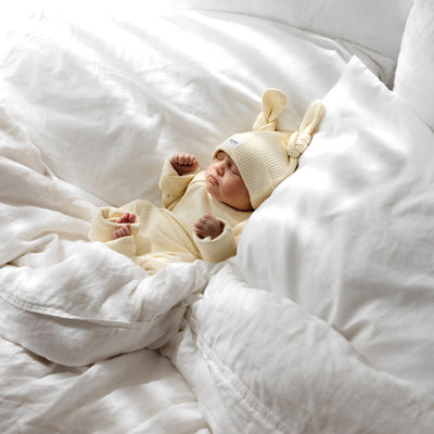 Baby in a lemon-colored outfit and hat lying on a white blanket