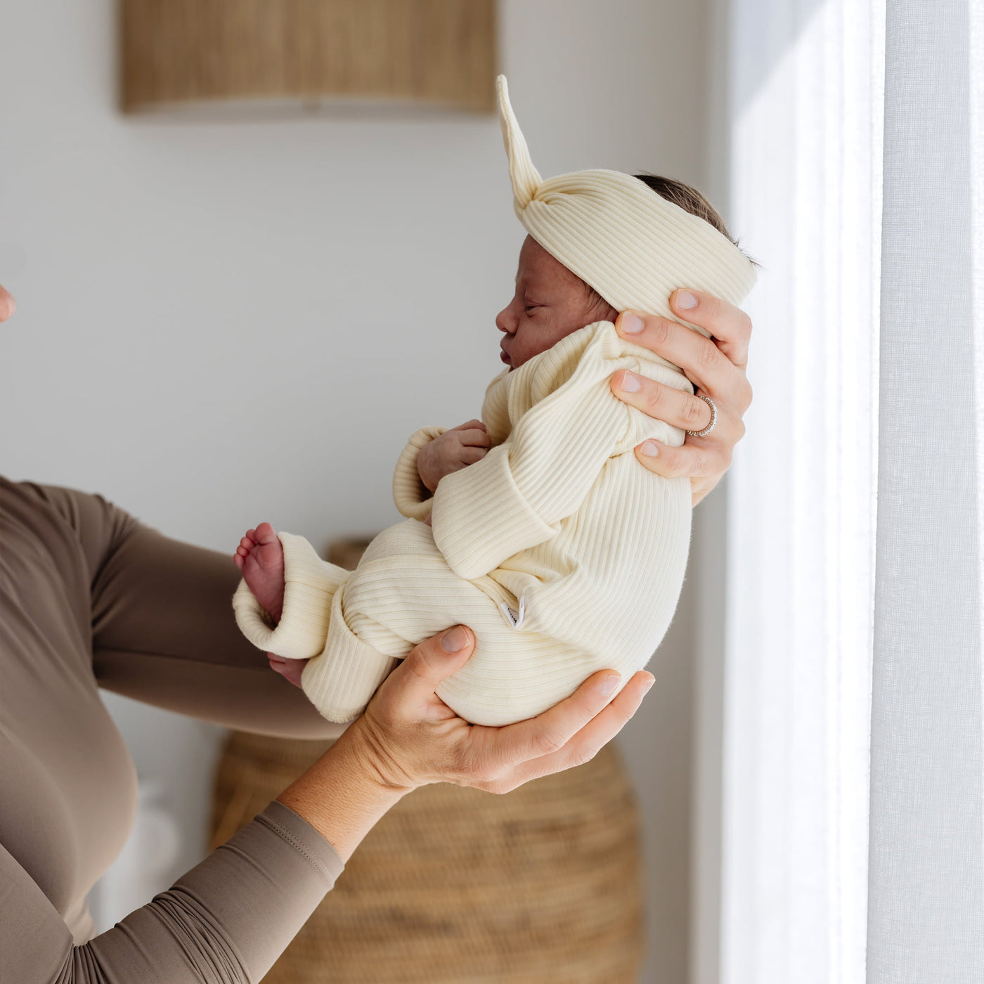 Newborn baby wearing matching yellow headband and onesie being held by a person in a neutral setting.