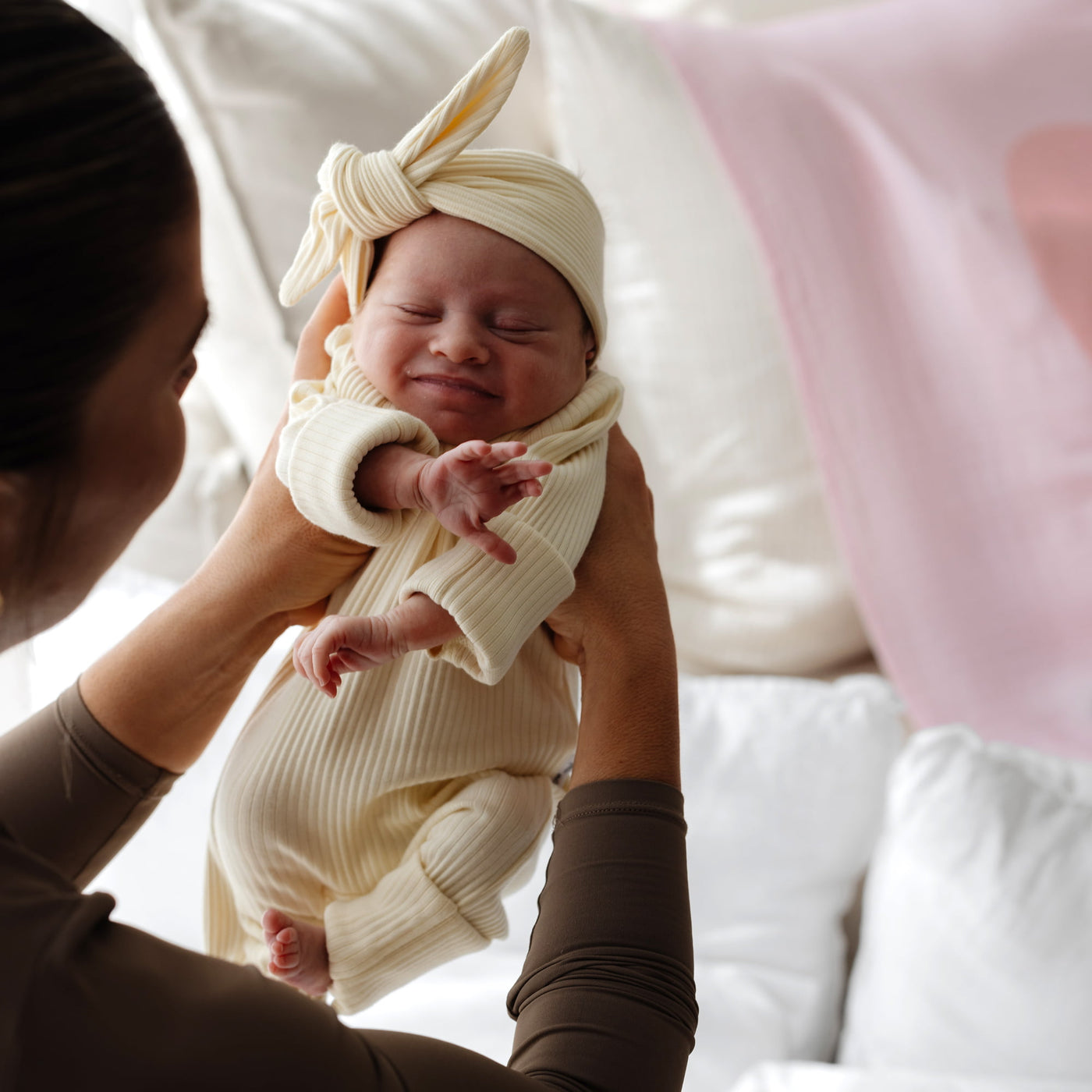 Baby in a lemon outfit and headband being held by a mother, with a blurred background