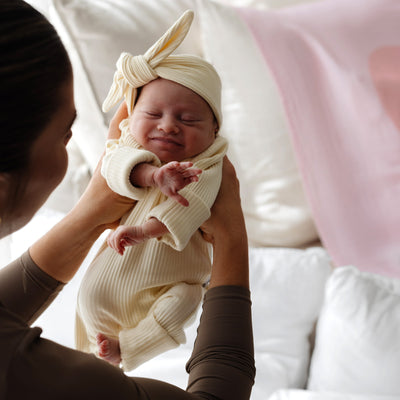 Baby in a lemon outfit and headband being held by a mother, with a blurred background
