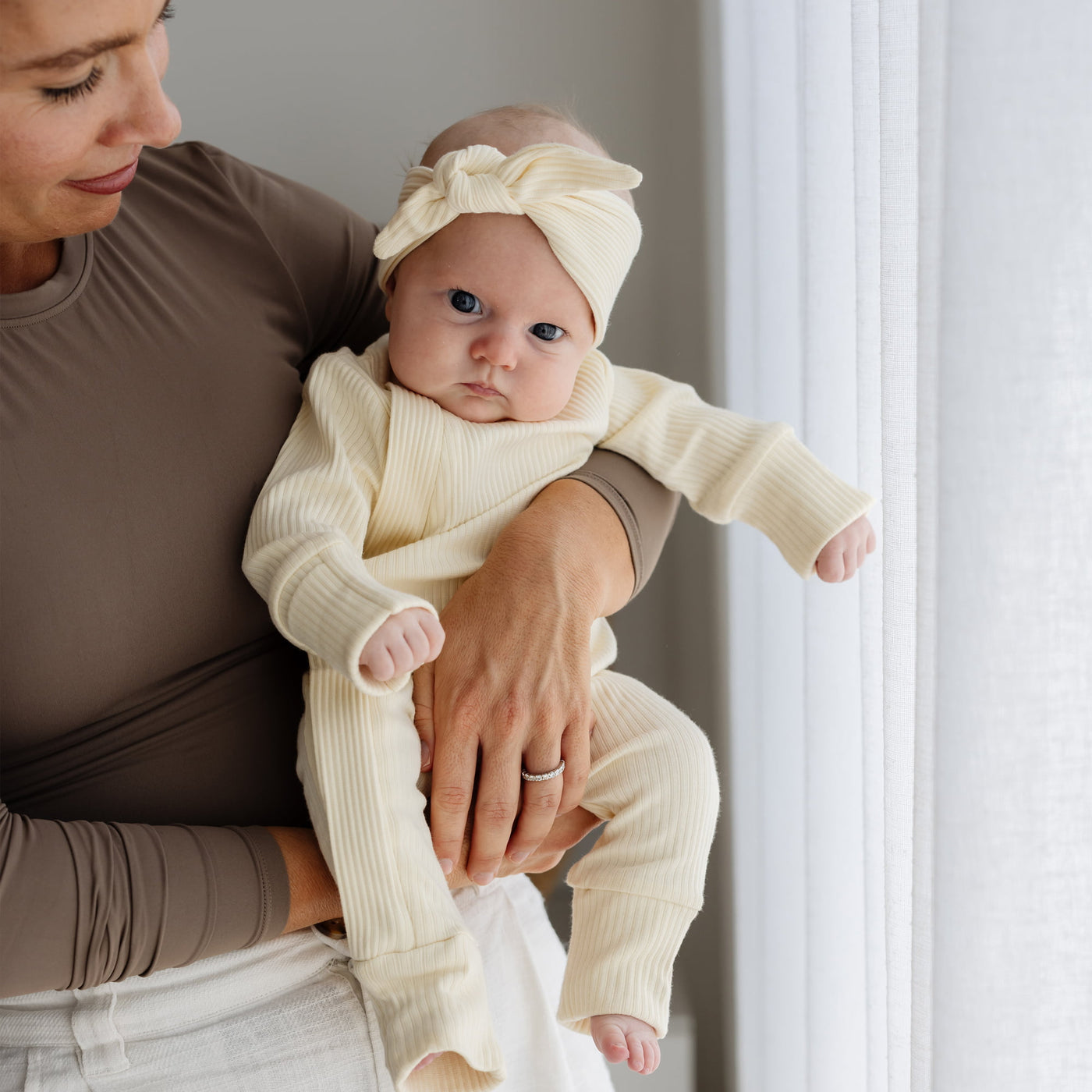 Woman holding a baby dressed in lemon clothing and headband against a neutral background