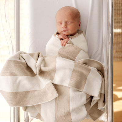 sleeping baby in clear bassinet wrapped in striped cotton blanket