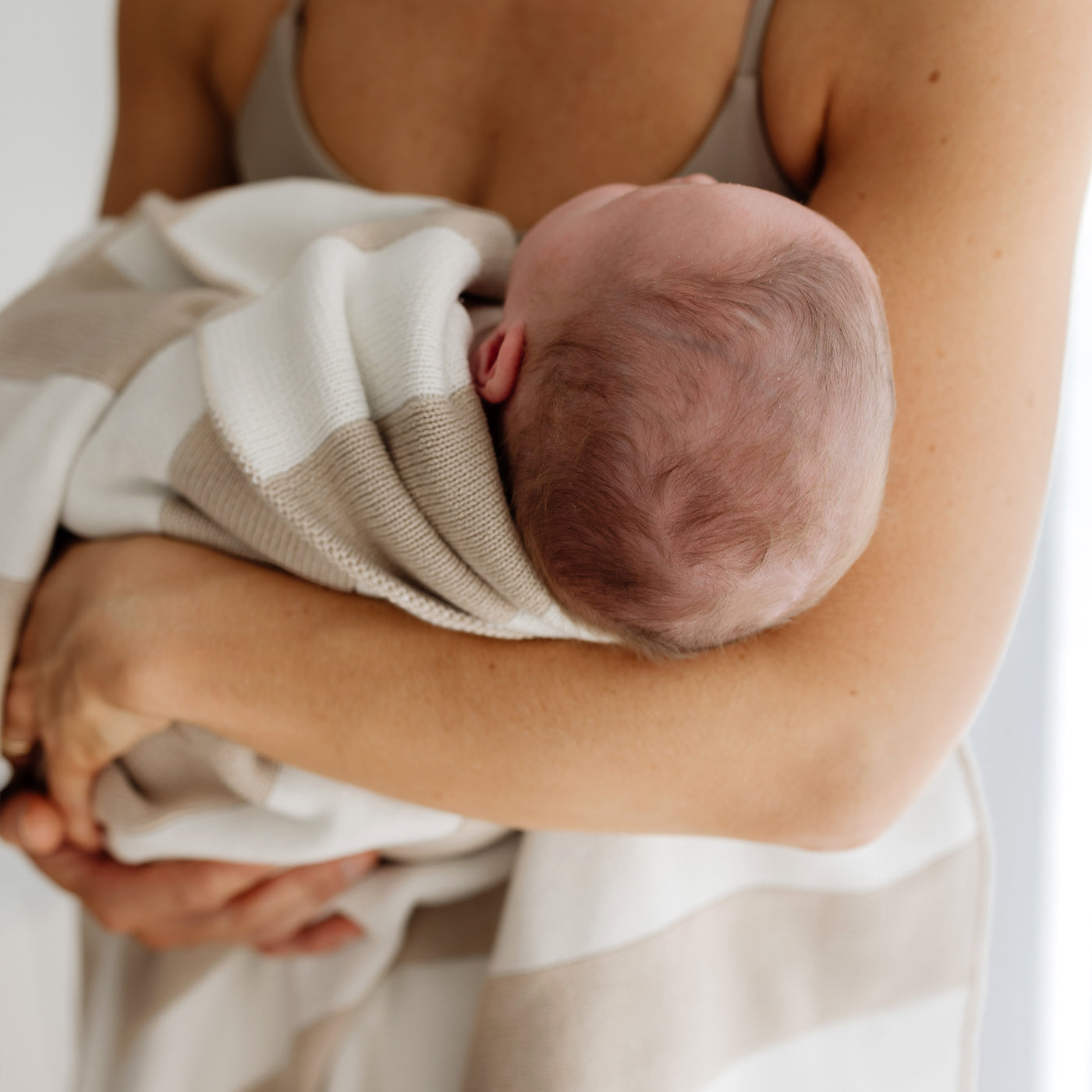 new born baby with hair held by mother in stripped knitted blanket