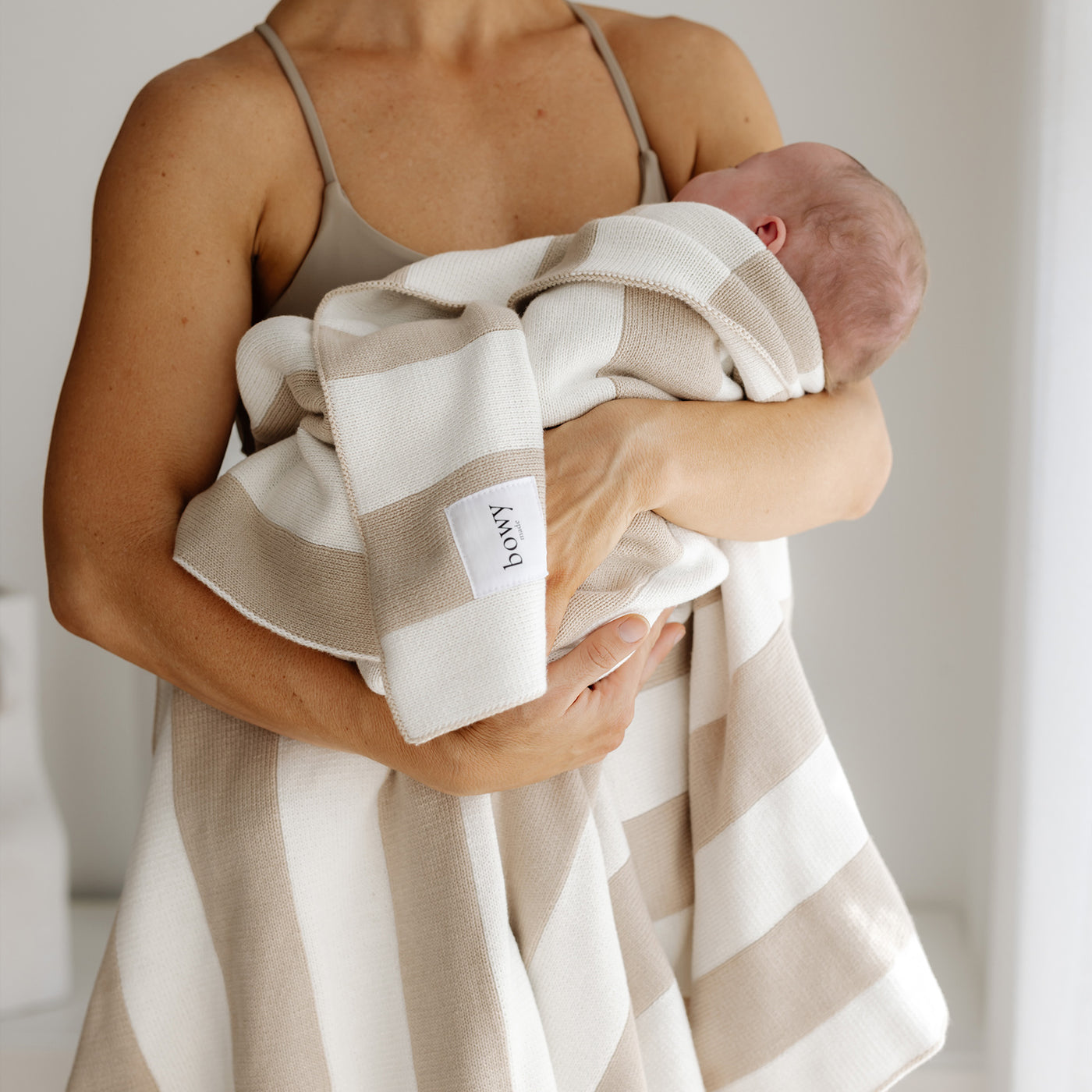 Mother hold newborn baby in white room with a knitted cream and white cotton blanket