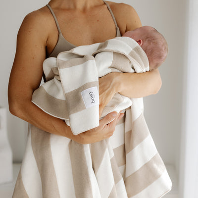 Mother hold newborn baby in white room with a knitted cream and white cotton blanket