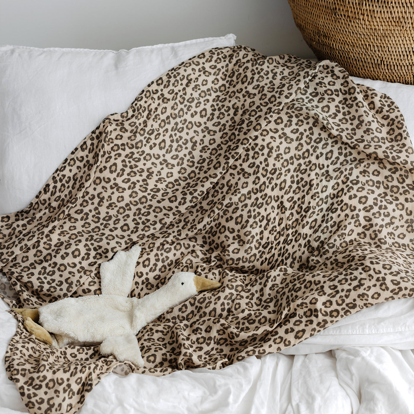 Leopard print blanket draped over a white pillow with a plush toy underneath.