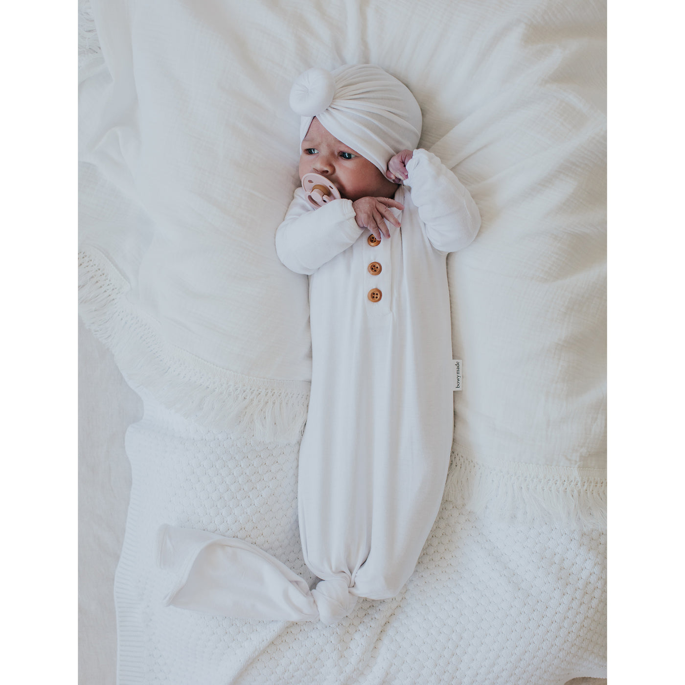 New born baby wearing white knotted gown on white sheets