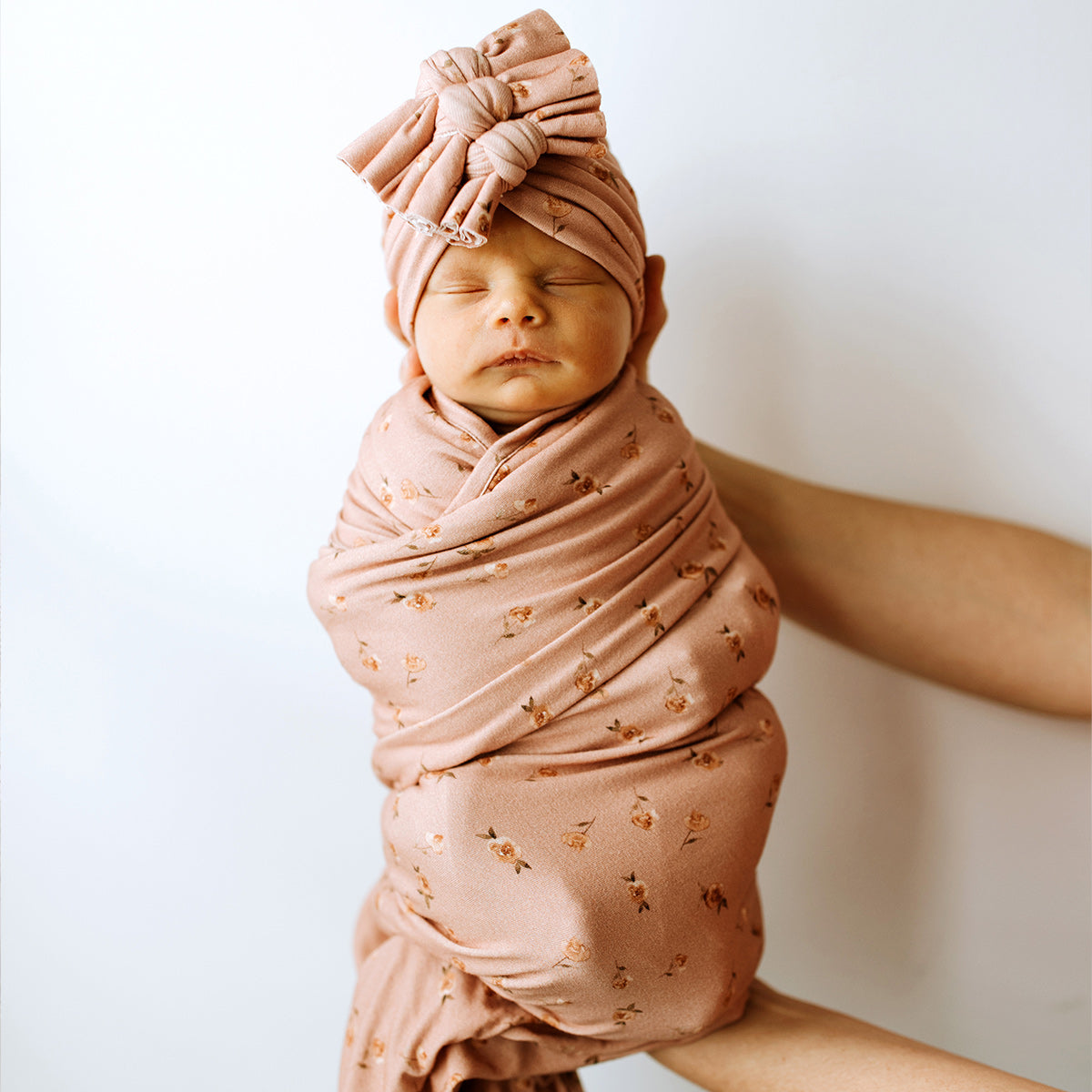 baby wearing tan floral swaddle and 3 bow beanie set
