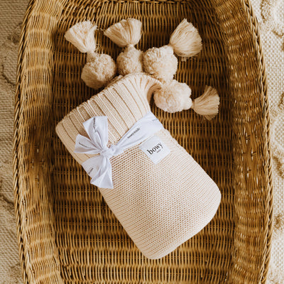 Cream Cotton Blanket with Pom Poms sitting in cane basket