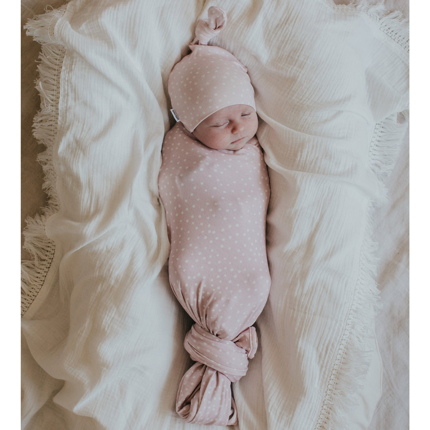 Cute newborn baby sleeping wearing matching pink dot swaddle and top knot beanie