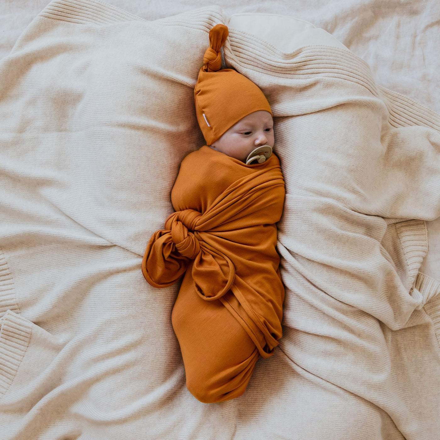Cute baby wrapped in mustard colour swaddle with matching top knot beanie