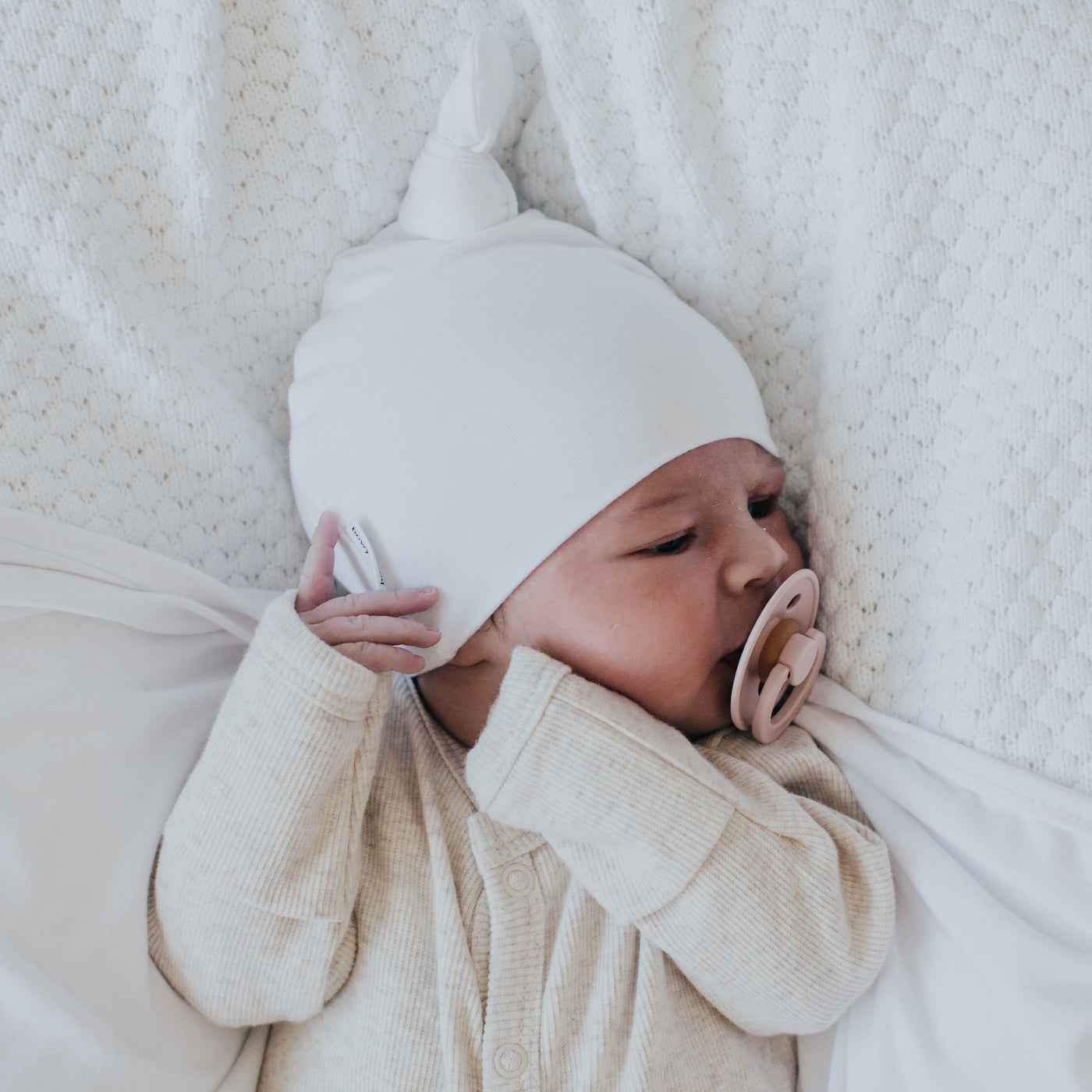 Baby dressed in white wearing white top knot beanie