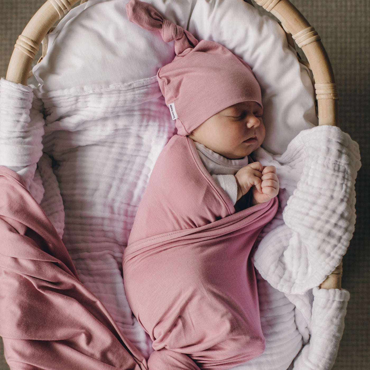 Cute bubb sleeping in bassinet wearing matching pink swaddle and top knot beanie