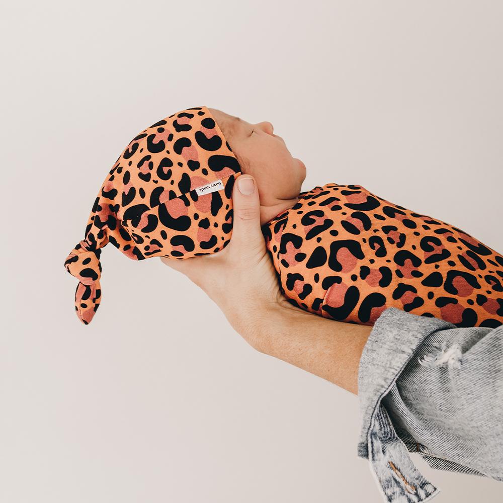 baby being held by mother wearing top knot beanie in leopard print
