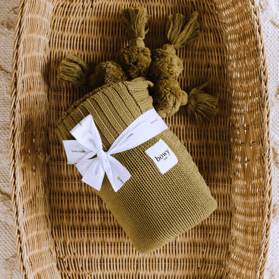 Green Cotton Blanket with Pom Poms sitting in cane basket
